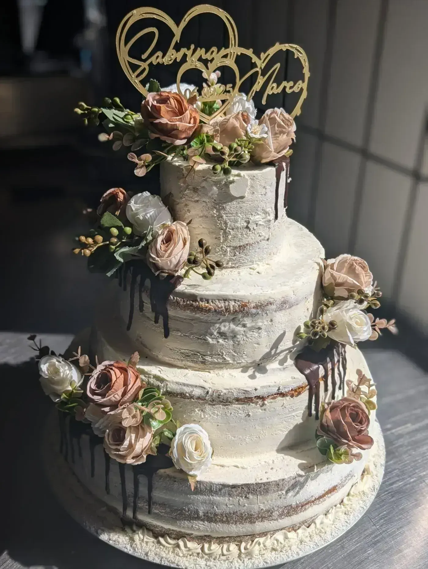 Dreistöckige Hochzeitstorte mit Rosen, Schokoladen-Drip und goldenem Namensschild des Brautpaars