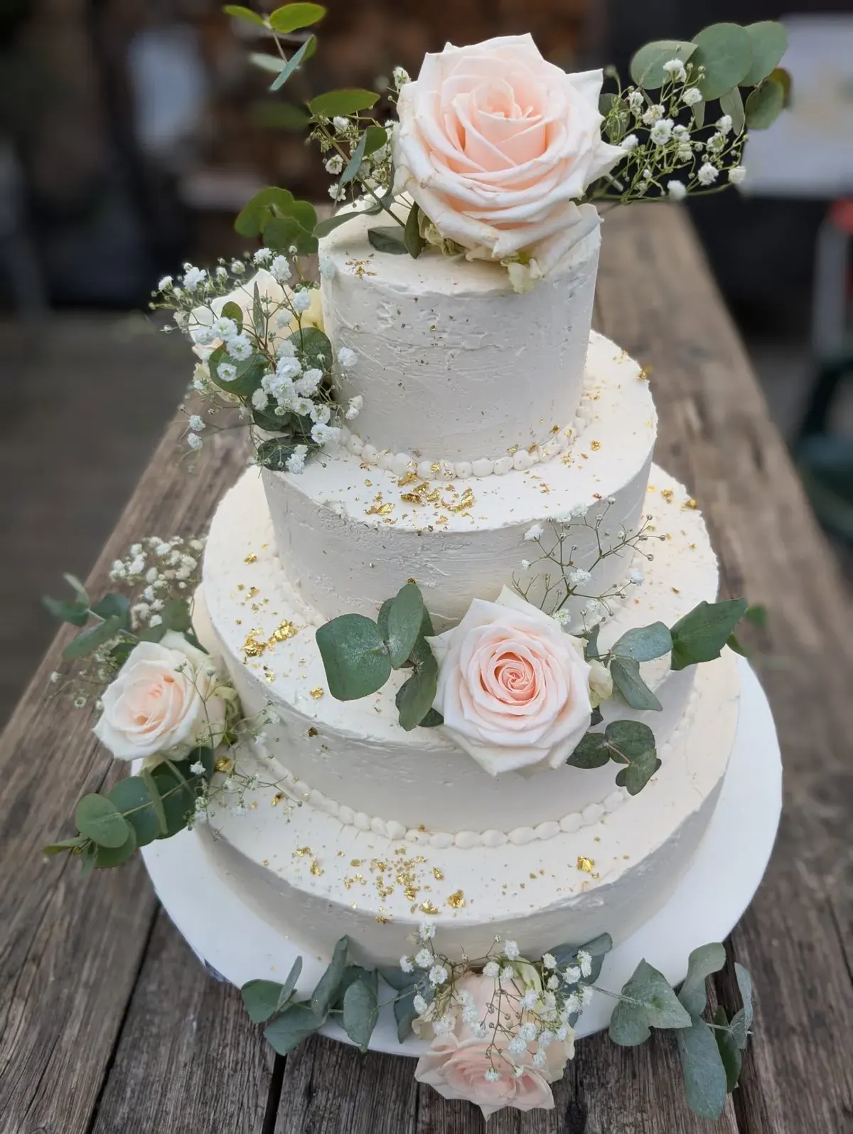 Dreistöckige weiße Hochzeitstorte mit Rosen, Eukalyptus und Blattgold aus dem Schürener Backparadies